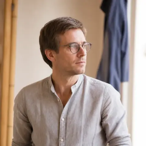 Retrato de Telmo Arrieta, pelo castaño corto y gafas de montura fina, camisa de lino gris, en una cocina clara