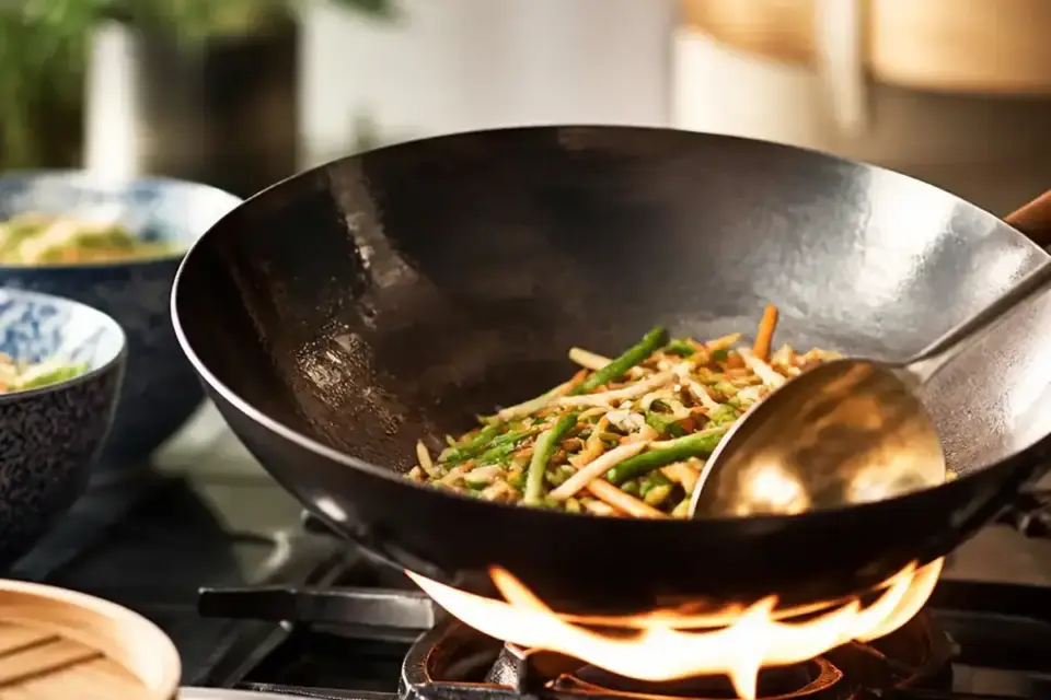 Un wok de acero con verduras salteadas y llamas bajo el wok en una cocina clara